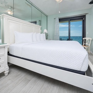 Master suite bedroom featuring a king bed, a TV, and a stunning view of the beach through sliding glass doors