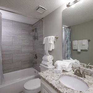 The guest bathroom features a tub/shower combo with a decorative curtain, granite countertop, and neatly arranged towels