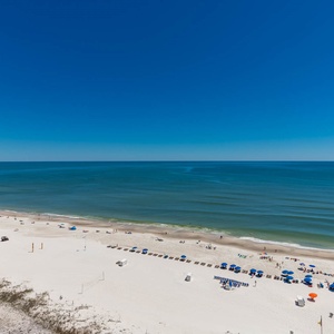 Pristine beach with white sand, dotted with colorful umbrellas and beachgoers enjoying the sun
