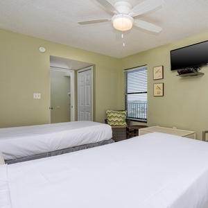 This guest bedroom features two beds, a TV, and a cozy seating area with a view of the vibrant outdoors