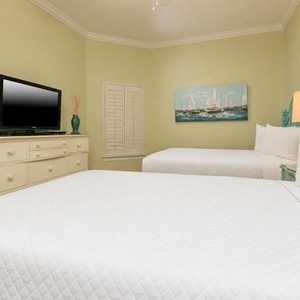 This guest bedroom features two comfortable queen beds, a TV for entertainment, and a serene sailing painting on the wall