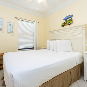 Guest bedroom featuring a queen bed, light yellow walls, beach-themed decor, and a bedside lamp for a relaxing atmosphere