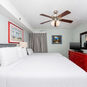 This cozy guest bedroom features a full and a twin bed, a vibrant red dresser, and a flat-screen TV for your entertainment