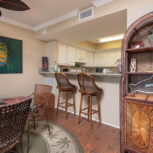 The dining area features a round glass table with woven chairs, a fish painting, and a stylish bar for entertaining