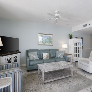 The living space features a teal sofa with decorative pillows, a striped chair, and a rustic coffee table