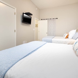 Relax in this inviting guest bedroom featuring two comfortable queen beds, coastal decor, and a TV