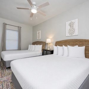 Guest bedroom featuring two queen beds with woven headboards, a stylish lamp, and cheerful pineapple wall decor
