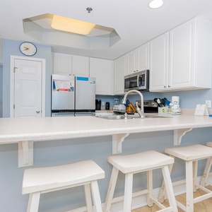 This bright kitchen features stainless appliances, white cabinetry, and a welcoming bar area with stools for casual dining
