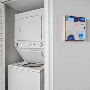 A compact laundry area features a stacked washer and dryer alongside two colorful abstract art pieces on the wall