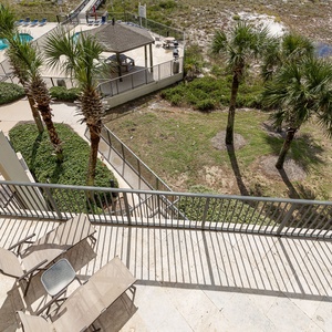 Balcony features comfortable seating and views of the pool area surrounded by lush palm trees and greenery