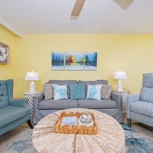 The living room features a gray sofa with queen sleeper, two accent chairs, and vibrant artwork against a yellow wall