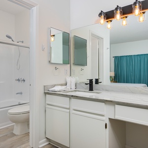 Bright and modern guest bathroom featuring a sleek vanity, glass tub/shower combo, and a glimpse of a cozy bedroom beyond