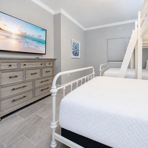 Inviting guest bedroom featuring a large TV, a stylish dresser, and a cozy lofted twin over queen bunk beds