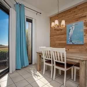 Dining area features a wooden table with white chairs, blue curtains, and a bird painting against a wood-paneled wall