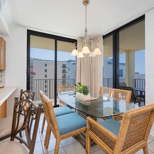 Dining area features a glass table surrounded by wicker chairs, with a view of the beach visible through sliding glass doors