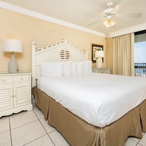 Master bedroom features a king bed, coastal-inspired furnishings, and a sliding door leading to a balcony with gulf views