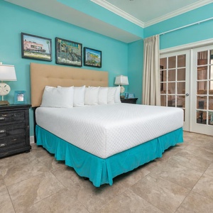The master bedroom features a cozy bed with white linens, turquoise accents, and French doors leading to a lovely view