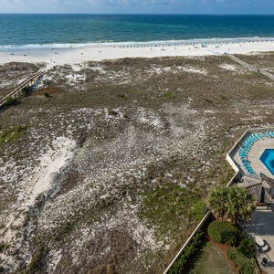 Balcony view of the beach, with white sand and turquoise waters, alongside a pool area featuring lounge chairs and a gazebo