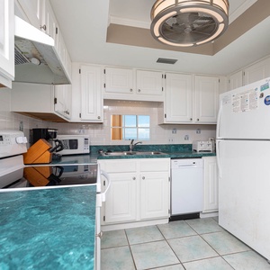 Bright kitchen featuring white cabinets, white appliances, and a sink mirror showcasing the lovely balcony view