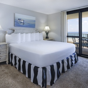 Master bedroom featuring a king bed with a striped skirt and a balcony offering views of the tranquil gulf waters