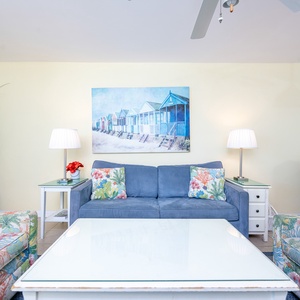 Brightly decorated living area features a blue sofa with colorful pillows, paired with floral armchairs and a coastal artwork
