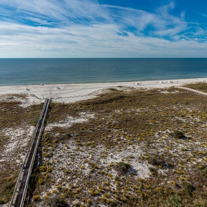 Impressive view of the beach and gentle waves, framed by lush greenery and a wooden boardwalk