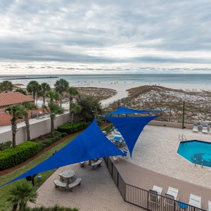 Enjoy the inviting pool area with shaded seating, lush greenery, and views of the tranquil shoreline beyond
