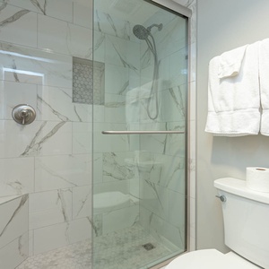 Glass-enclosed walk-in master shower with sleek tile design and plush white towels hanging nearby, creating a refreshing vibe