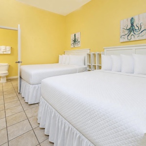Bright yellow walls complement two queen beds with white linens, creating a cheerful atmosphere in this inviting guest room