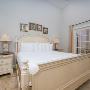 The master bedroom features a light-colored wooden king bed, elegant decor, and a view of the dining and balcony area