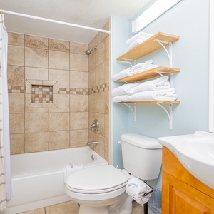 Bright and inviting guest bath featuring a tub/shower combo, neatly arranged towels, and warm wooden accents