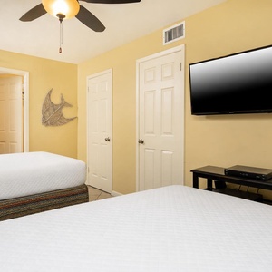 Cheerful guest bedroom featuring two comfortable queen beds, a TV, and vibrant decor for a relaxing stay