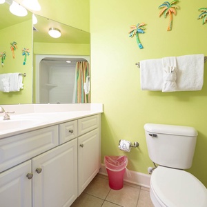 Cheerful guest bathroom featuring vibrant green walls, a spacious vanity, and colorful striped shower curtains