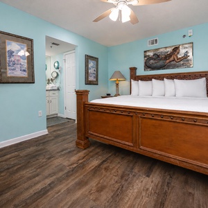 Cozy master bedroom features a wooden king bed with plush white bedding, soft turquoise walls, and an en-suite bathroom