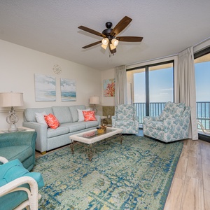 Relax in the airy living room, featuring a plush sofa and chairs, with beautiful beach views from the balcony