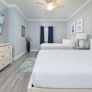 Serene guest bedroom featuring two queen beds, a large TV, and charming art and design