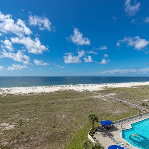 Stunning view of the beach, lounge chairs, and a sparkling pool area under a clear blue sky