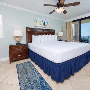 The master bedroom features a large king bed with crisp white linens, coastal decor, and a lovely view from the balcony