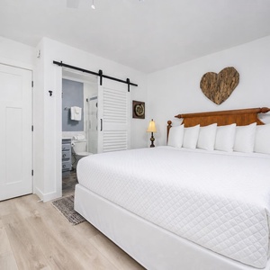 This cozy bedroom features a king-size bed with soft white linens, and a charming heart-shaped decor piece on the wall