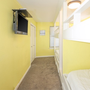 Cozy bunk room including four queens, featuring a mounted TV and a cheerful atmosphere for relaxation