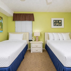 This guest bedroom featuring two beds, a double and a twin, vibrant green walls, and beach artwork for a relaxing stay