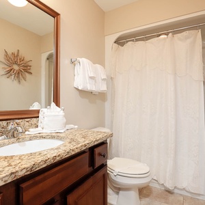 This bathroom features a stylish granite countertop, elegant mirror, and a relaxing shower with a decorative curtain