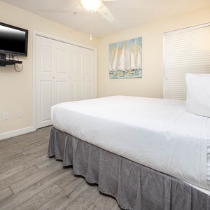 Guest bedroom featuring a queen bed, wall-mounted TV, and serene nautical artwork for a relaxing getaway