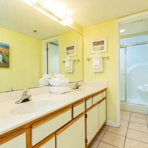 Bright yellow walls complement the dual sink vanity, while a walk-in shower is visible through the door on the right