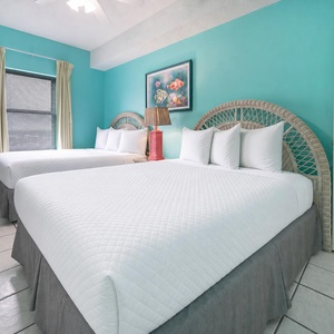 Two queen beds with white linens are featured in this guest bedroom, creating a cheerful atmosphere