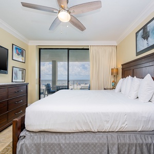 The master bedroom features a king-size bed, a TV, and a stunning beachfront view through sliding glass doors