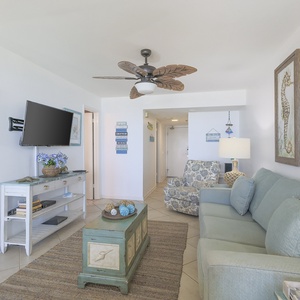 Living area featuring a light blue sofa with queen sleeper, a decorative coffee table, and TV, complemented by coastal decor