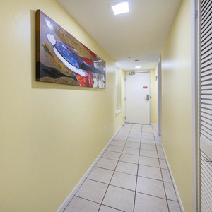 Brightly painted hallway featuring tiled flooring and a colorful abstract painting, leading to the entrance of the unit