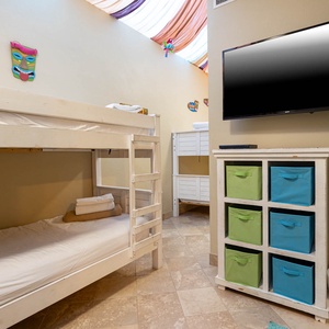 Two twin bunk beds with colorful decor and a wall-mounted TV create a fun atmosphere in this cheerful indoor patio space