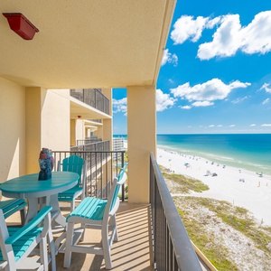 A turquoise table and chairs set on the balcony offers a perfect spot to enjoy the beach view and vibrant blue sky